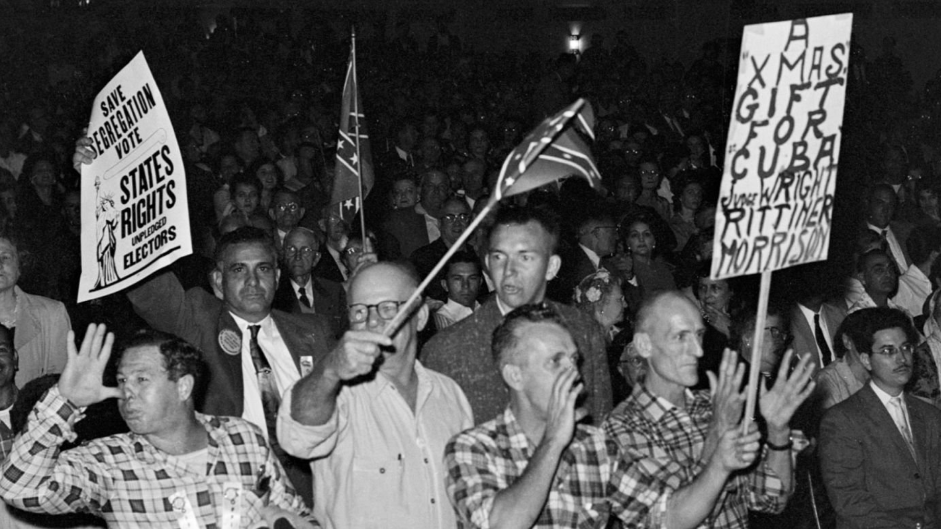 A group of white men cheering and jeering at a gathering. One man holds a sign that reads "Save Segregation Vote / States Rights"